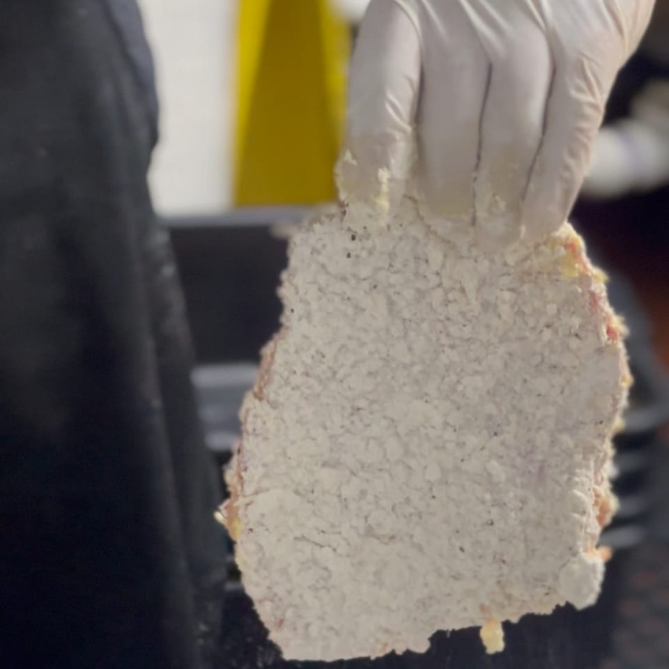 A gloved hand holds a piece of meat coated in white breading, ready for frying at Alyce cafe.