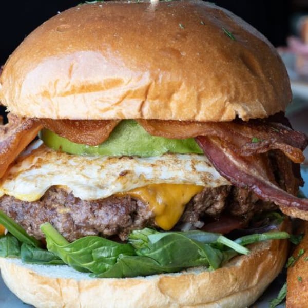 A close-up of Alyce's breakfast burger with bacon, avocado, fried egg, cheese, and spinach.