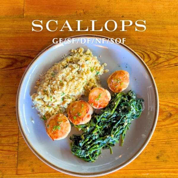 Seared scallops with cauliflower rice and sautéed spinach on a light gray plate.