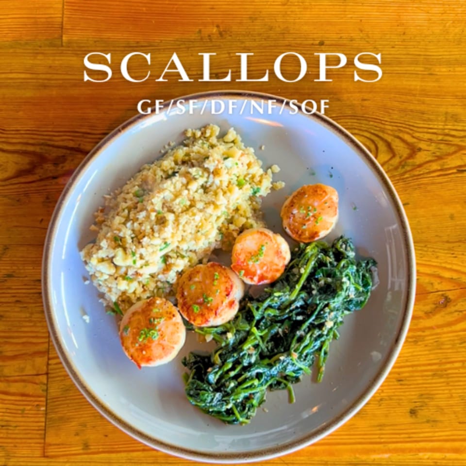 Seared scallops with cauliflower rice and sautéed spinach on a light gray plate.