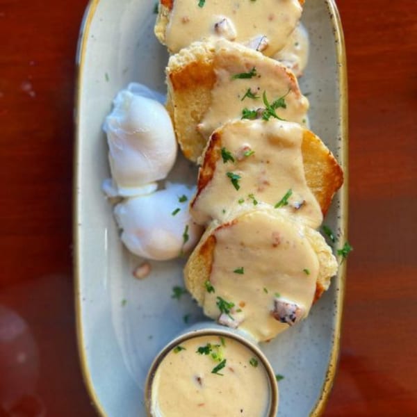 Alyce's biscuits and gravy with poached eggs and a side of gravy on a light blue plate.