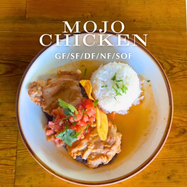 Mojo Chicken dish with rice, salsa, and plantain chips in a bowl on a wooden table.