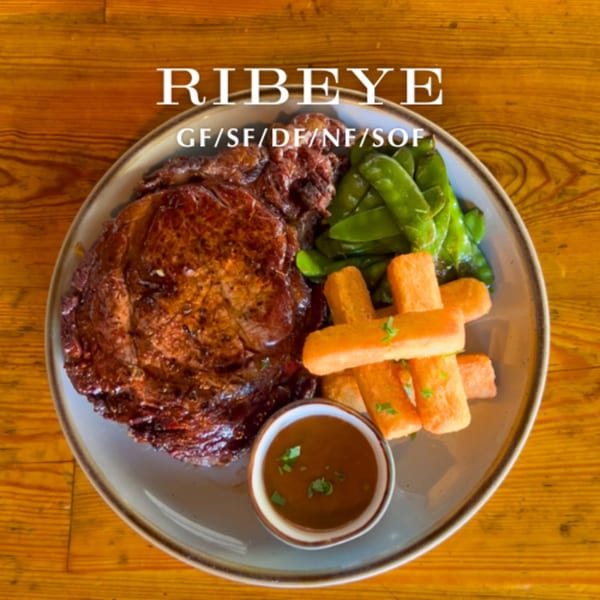 Alyce cafe's ribeye steak with green beans, fries, and a side of sauce on a wooden table.