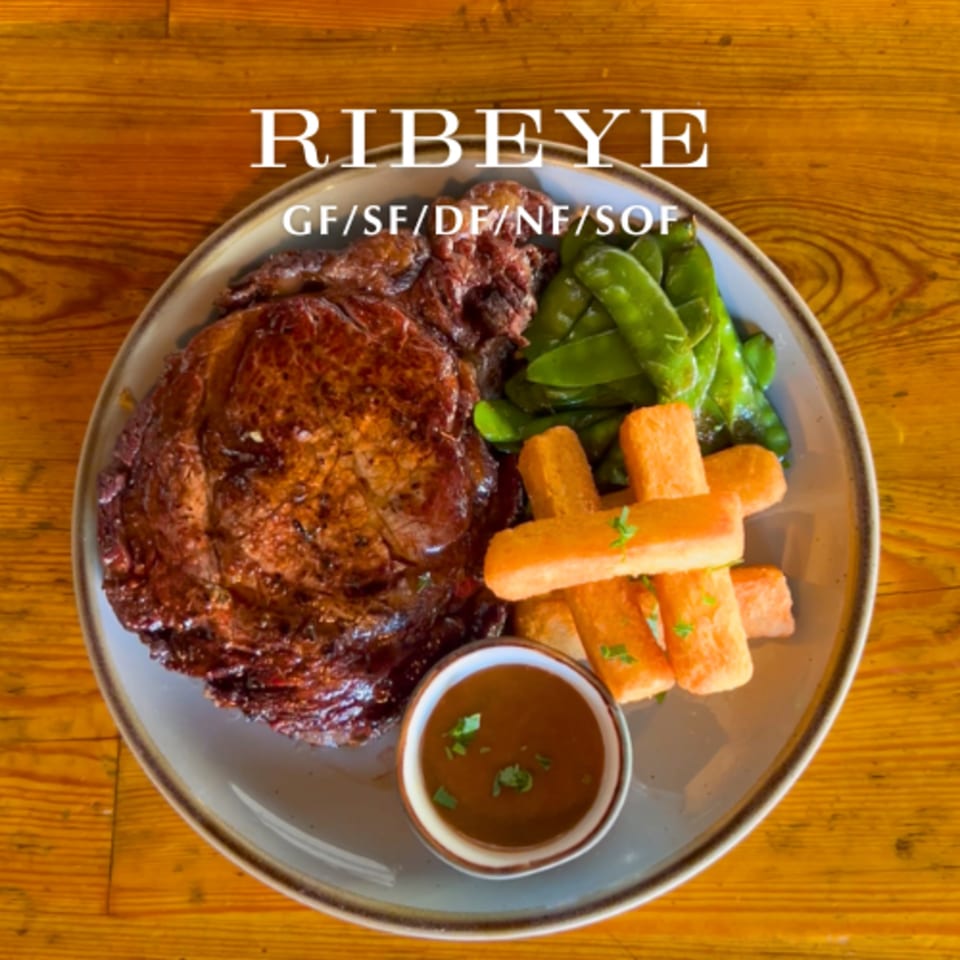 Alyce cafe's ribeye steak with green beans, fries, and a side of sauce on a wooden table.