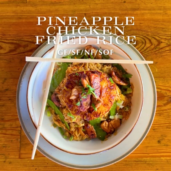 Pineapple chicken fried rice with green vegetables and chopsticks in a bowl on a wooden table.