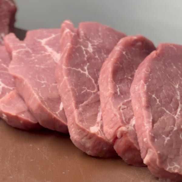 Several raw, thinly sliced cuts of pink meat with white marbling are arranged on a brown surface.