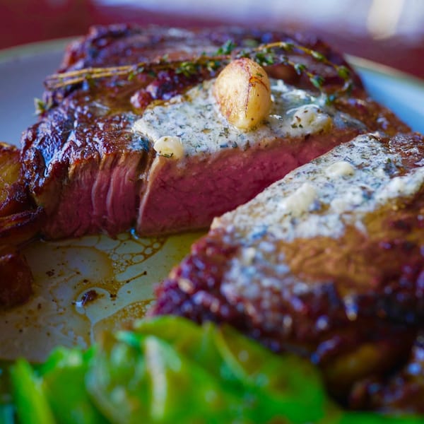 A perfectly cooked steak, sliced to reveal its pink interior, topped with melting herb butter and garlic.