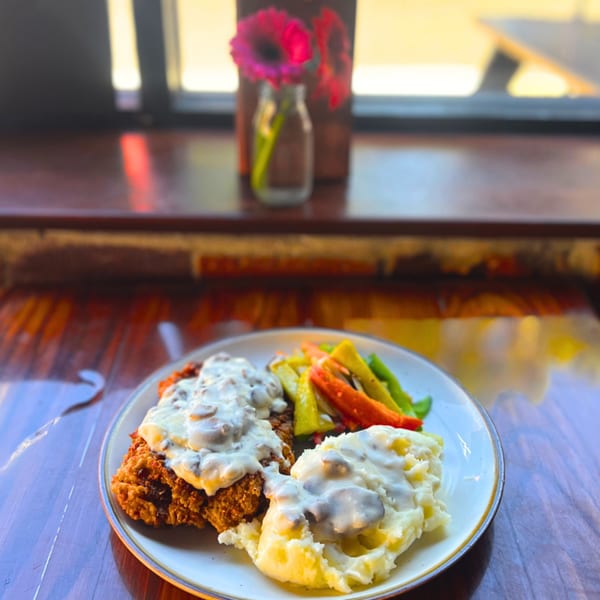 Alyce's chicken fried steak with mashed potatoes, gravy, and mixed vegetables on a wooden table.