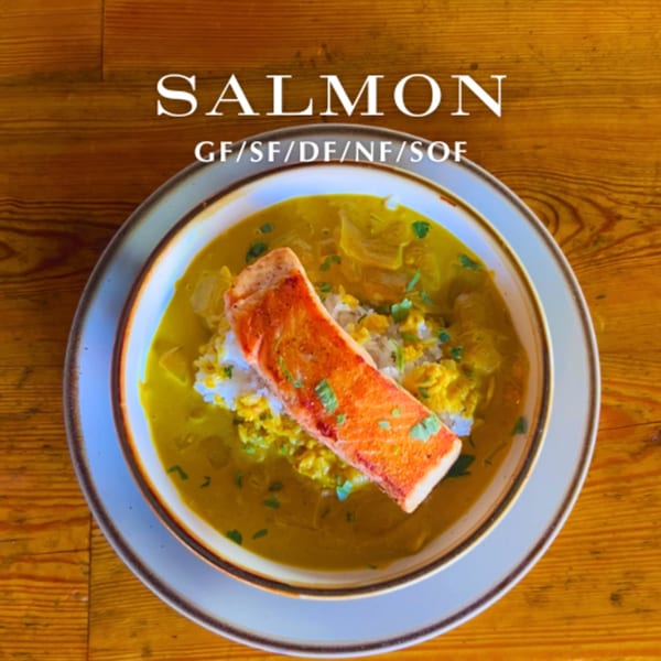 Alyce's salmon dish with rice and yellow curry, garnished with cilantro, on a wooden table.