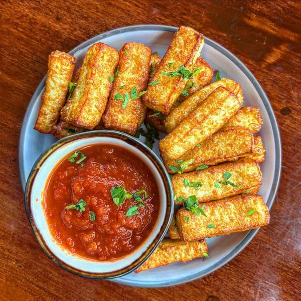 Golden-brown fried halloumi sticks with fresh parsley, served with a side of red marinara sauce.