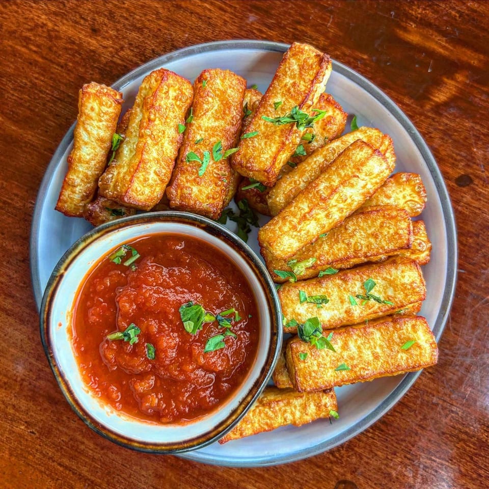 Golden-brown fried halloumi sticks with fresh parsley, served with a side of red marinara sauce.